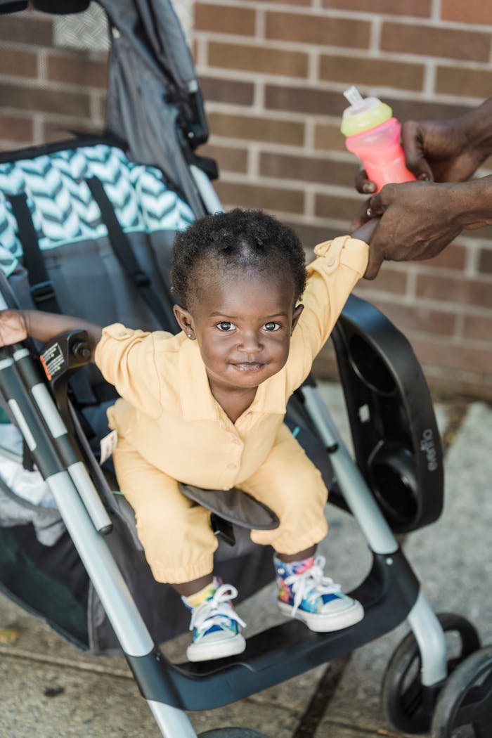 Offerings Adorable child in yellow outfit sitting in a pram, smiling while holding a parents hand.