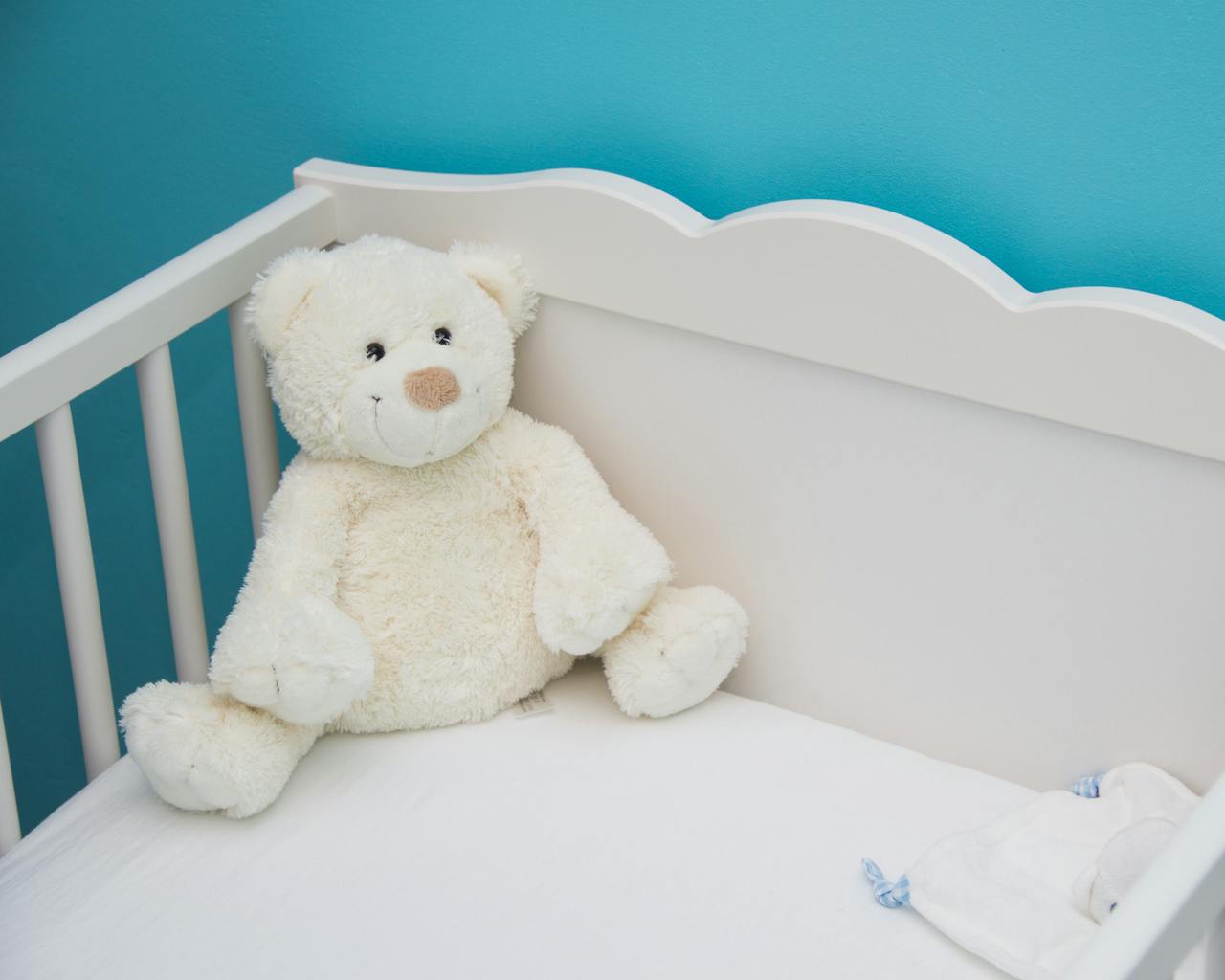 Home Soft teddy bear in a white crib against a vibrant blue wall, creating a comforting nursery atmosphere.